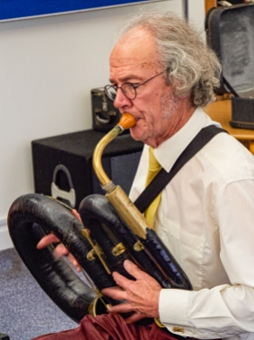 Man blowing into an old musical instrument known as a serpent.